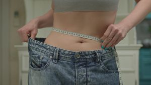 close up of woman measuring her waistline wearing oversized jeans after weight loss me SBI 351154798
